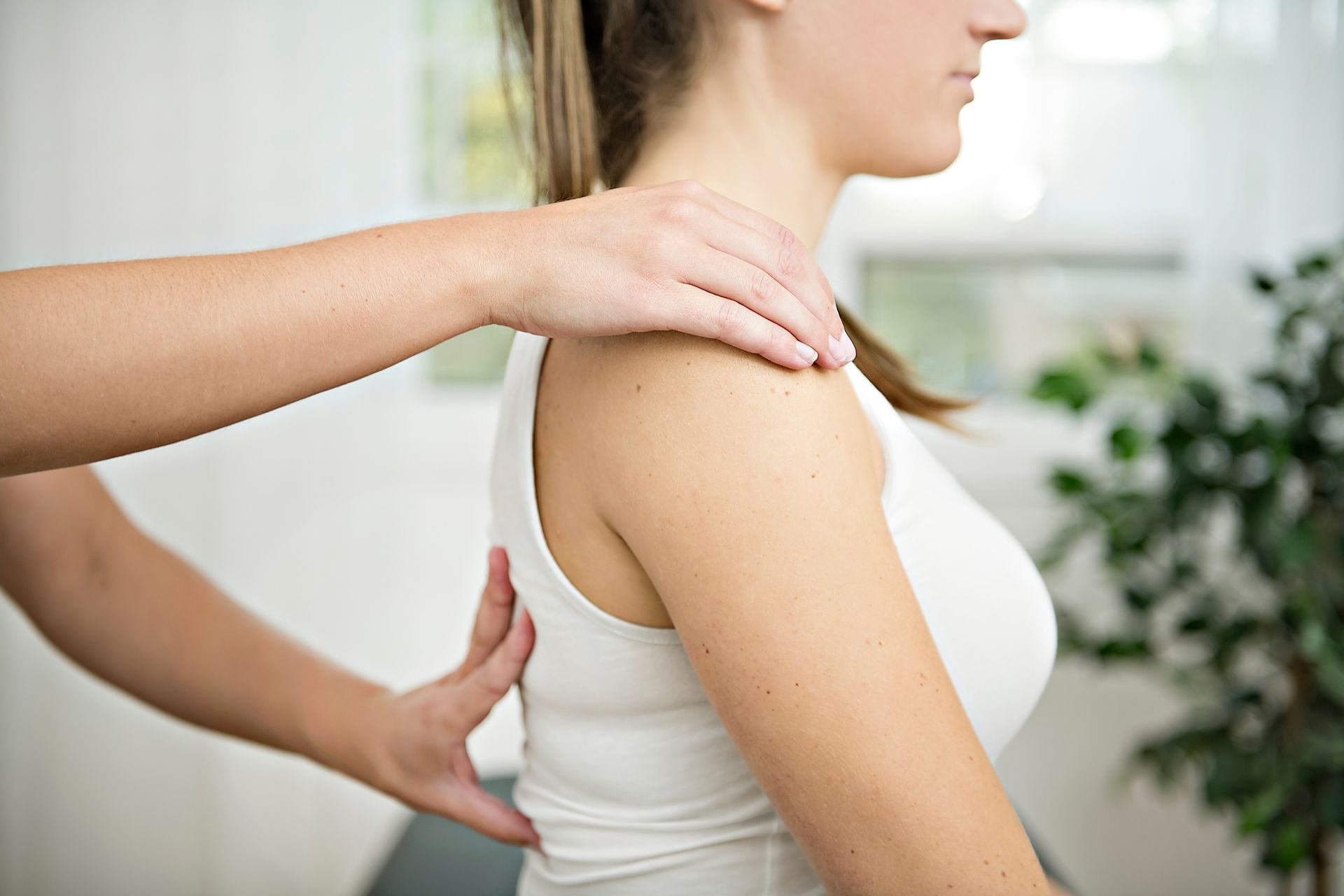 Physical therapist guiding a woman's shoulder and back posture in a bright clinic