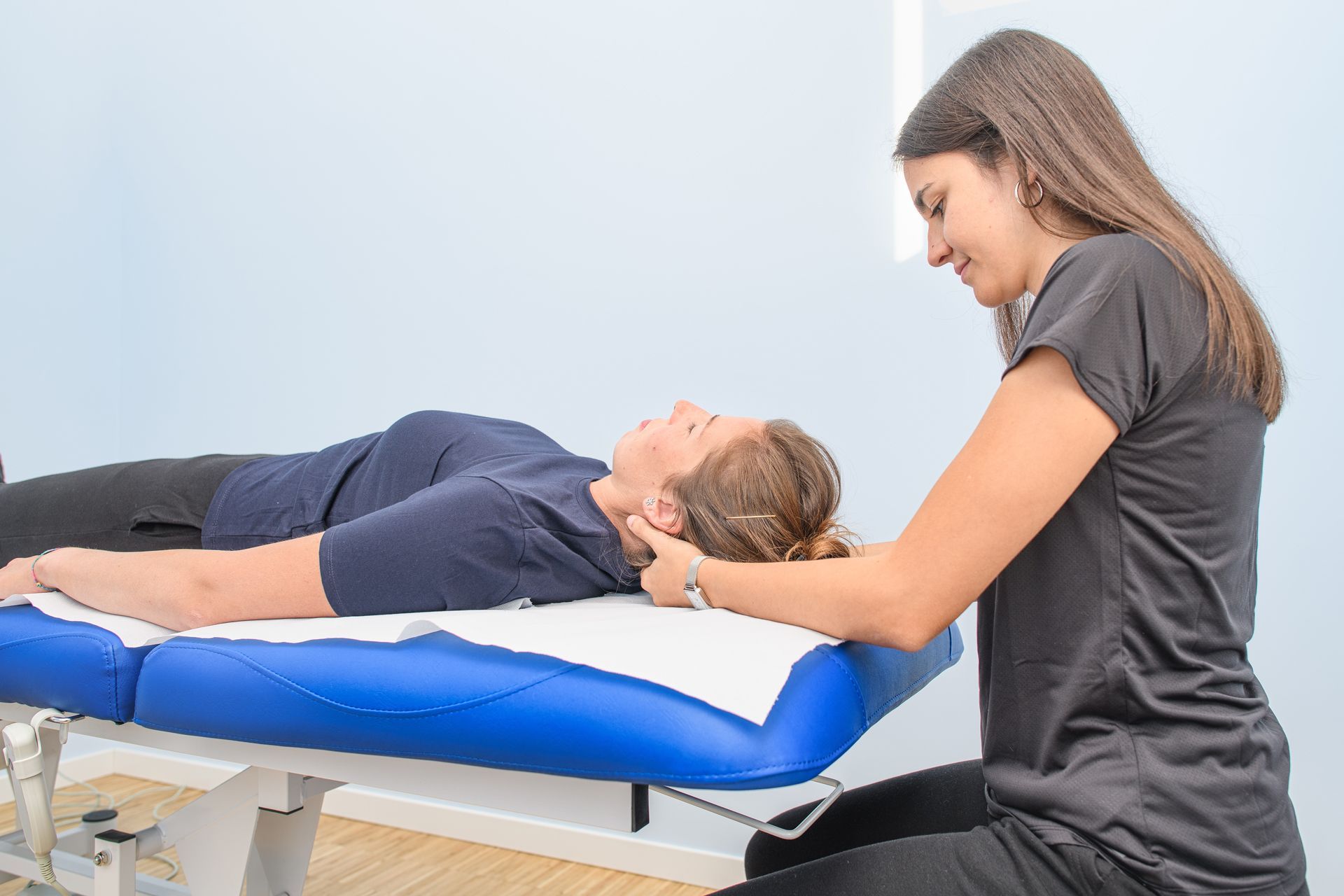 Therapist examining a patient lying on a blue treatment table in a clinical setting
