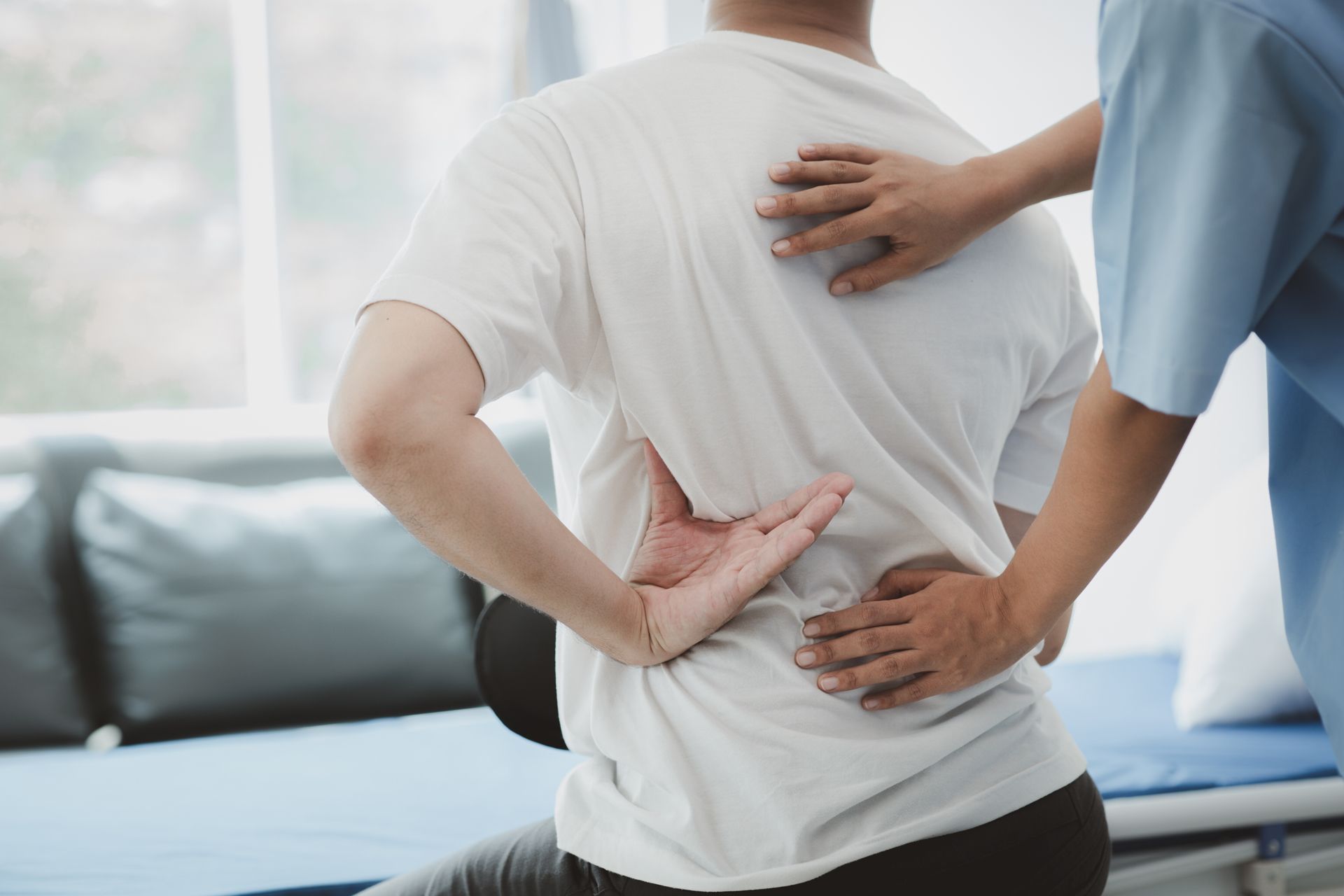 Physical therapist supporting a seated patient’s lower back during treatment indoors