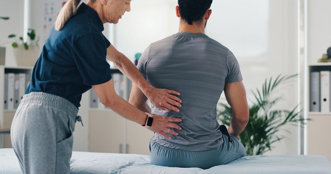 Therapist supporting a seated patient’s back during a physical therapy session in a bright clinic