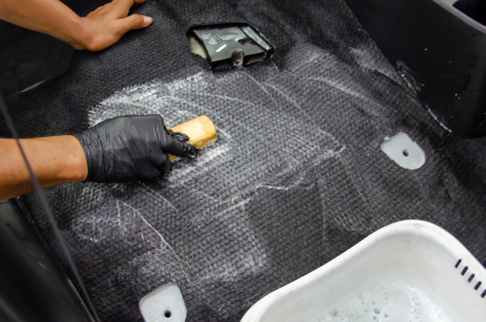 A person is cleaning the carpet of a car with a sponge.