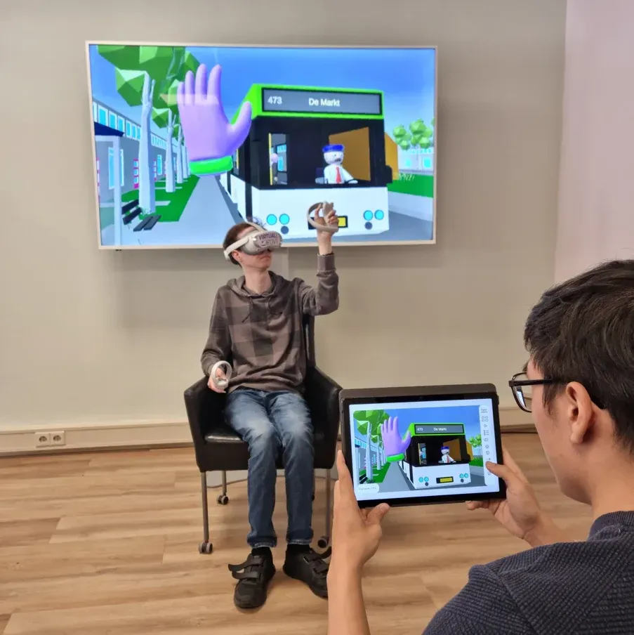 Een deelnemer oefent met Virtual OV met een VR-bril en controllers, terwijl een begeleider via een tablet meekijkt.