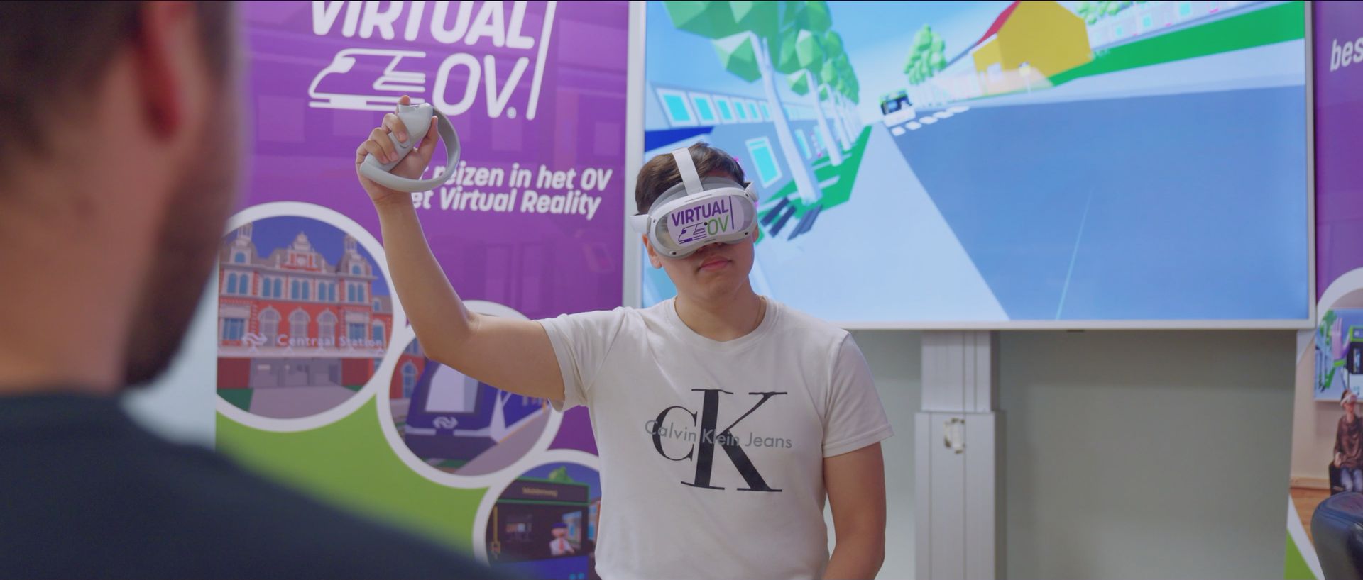  Een deelnemer oefent met Virtual OV op een VR-bril, terwijl een begeleider via een tablet meekijkt 