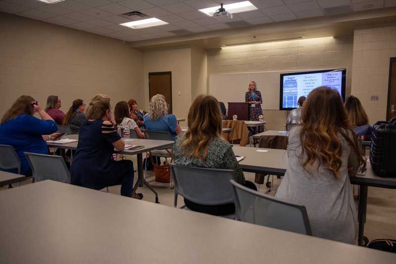 A woman presenting to a group in a brightly lit classroom. 