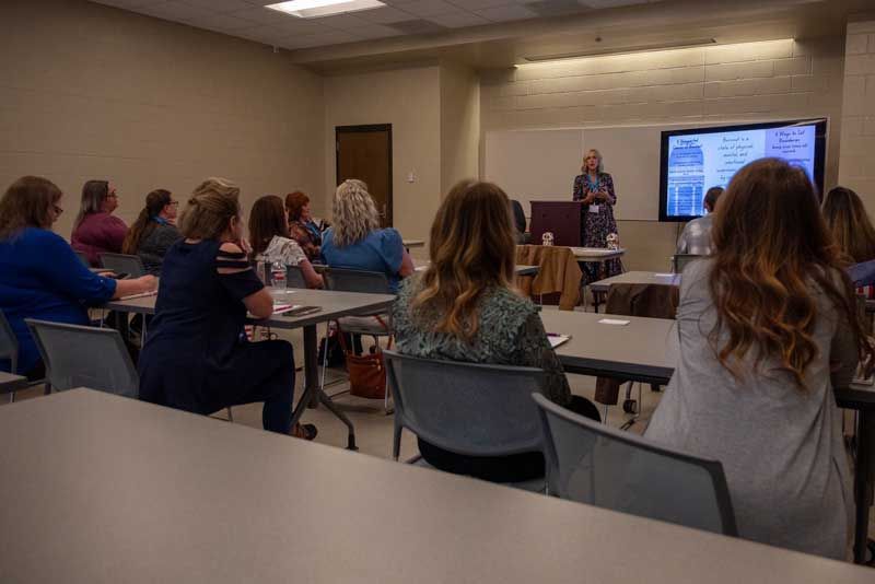 A woman lectures in a conference room with an audience.