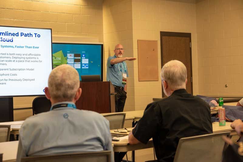 Man presenting in front of an audience; a screen with text and diagrams is behind him.