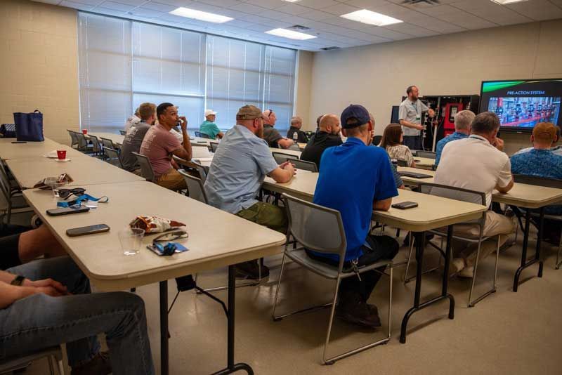 People in a classroom setting; a man lectures in front of a screen displaying an image.