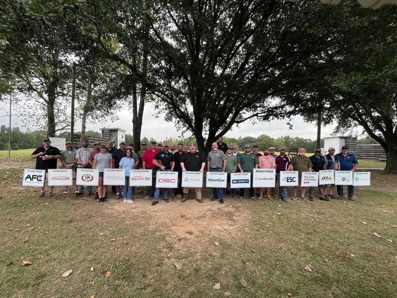 Group of people holding company signs outdoors under a tree.
