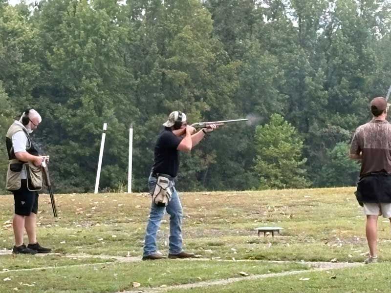 Three people shooting clay pigeons outdoors. 