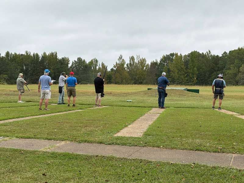 People shooting clay targets at an outdoor range, overcast sky.