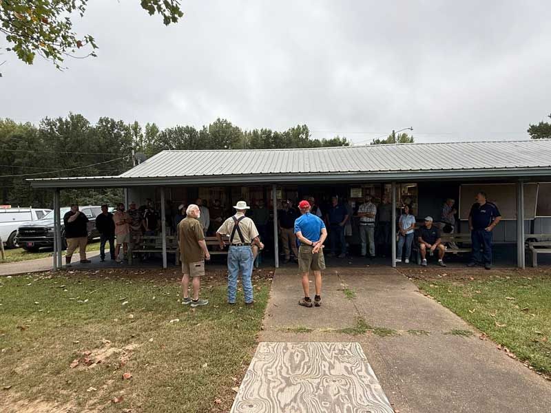 People gathered outside a low building with a metal roof. 