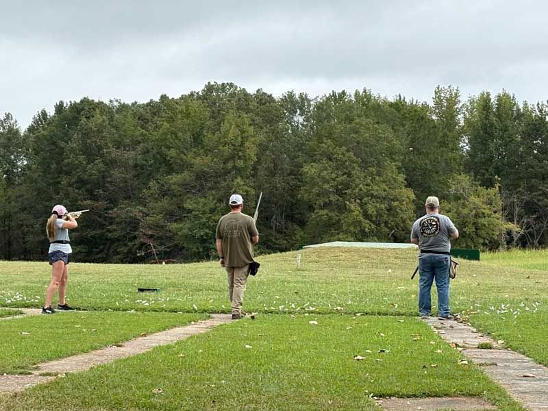Three people at a skeet shooting range on a cloudy day. 