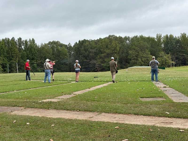 People shooting clay pigeons at an outdoor shooting range on a cloudy day.