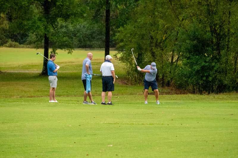 Four men playing golf on a green course.