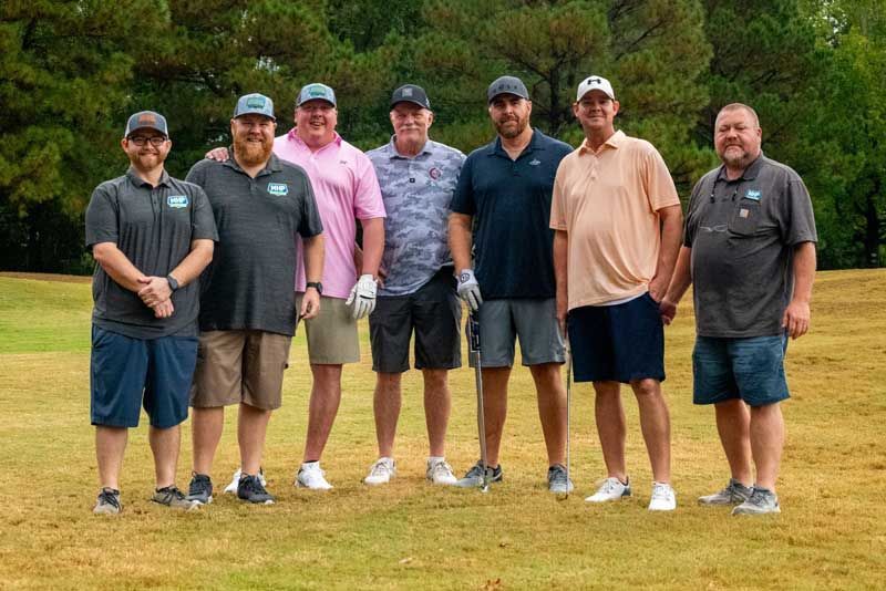 Group of seven men standing on a golf course.