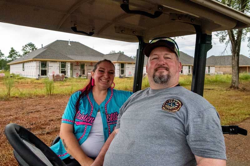 Couple in golf cart smiles in front of new homes under construction.