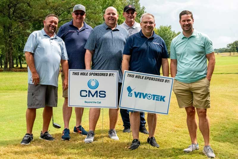Group of men holding signs at a golf course, sponsored by CMS and Vivotek.