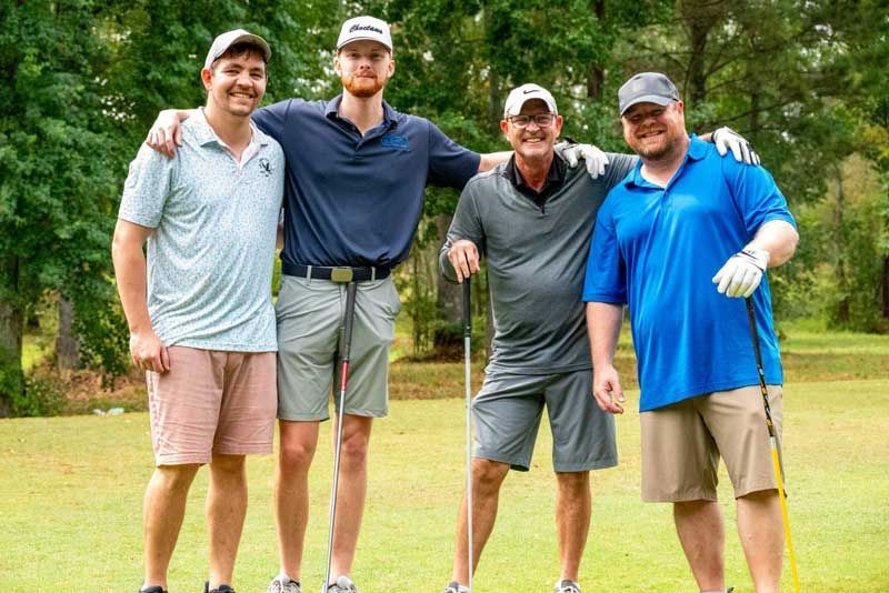 Four men smiling on a golf course, arms around each other.