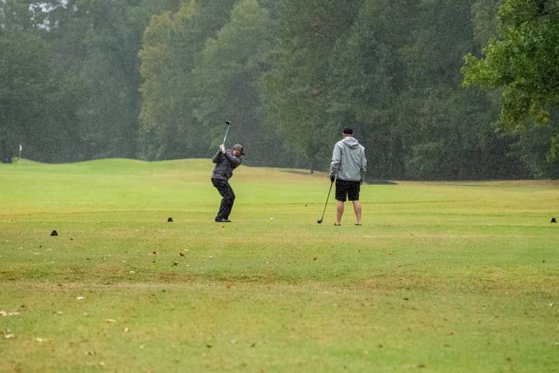Two golfers playing on a green golf course in the rain. 