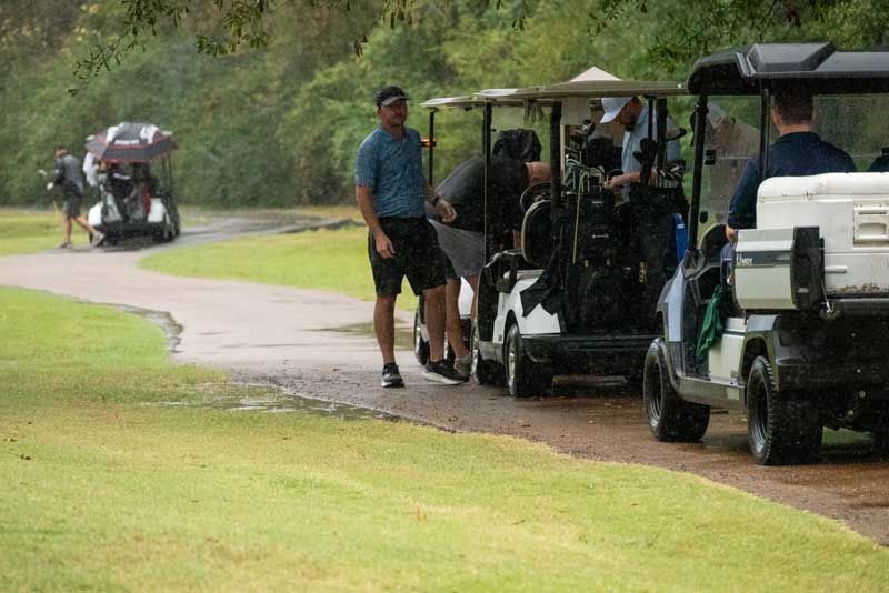 Golfers in golf carts during a rain storm on a golf course.