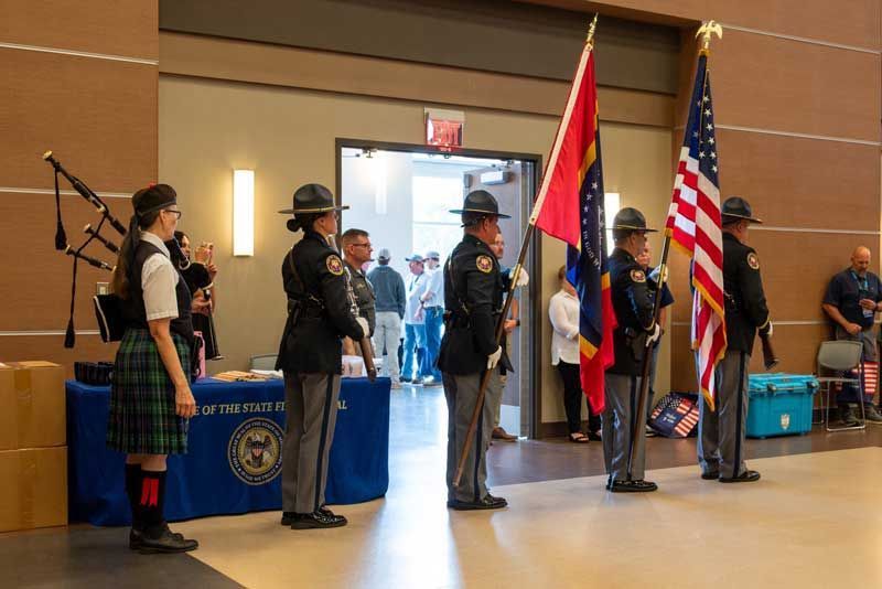 Color guard and bagpiper at an event, with flags and uniformed officers in a large hall.
