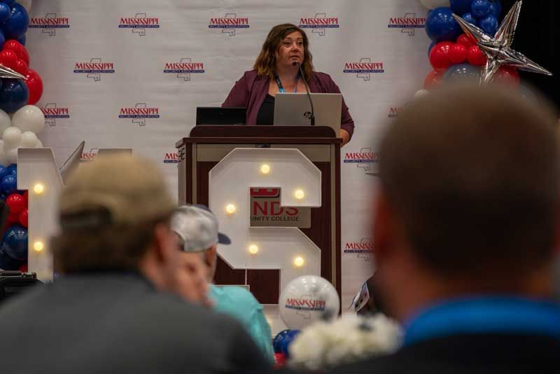 Woman speaking at a podium with a laptop. 