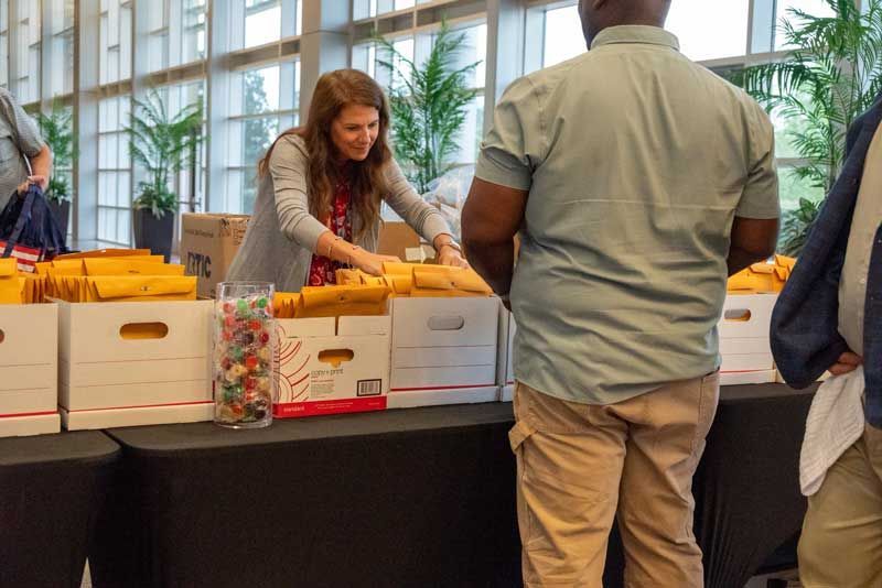 Woman behind a table with boxes of materials, assisting a person. 