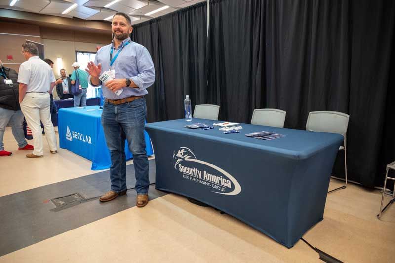 Man in blue shirt and jeans stands at a table.