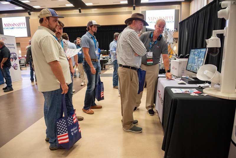People at a trade show booth, looking at a security camera display.