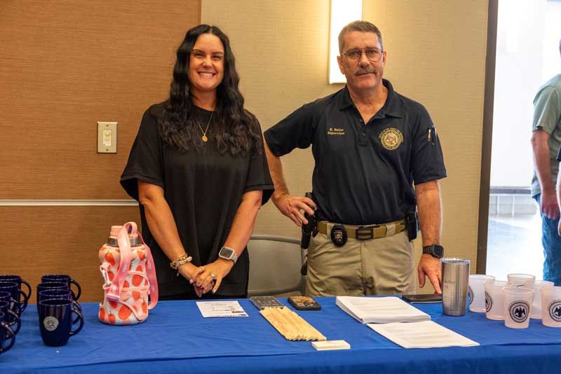 Woman and man at a table with promotional items. The man is wearing a uniform.