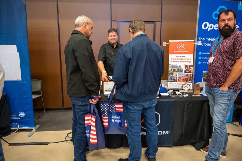 People at a trade show booth, viewing information on a table. 