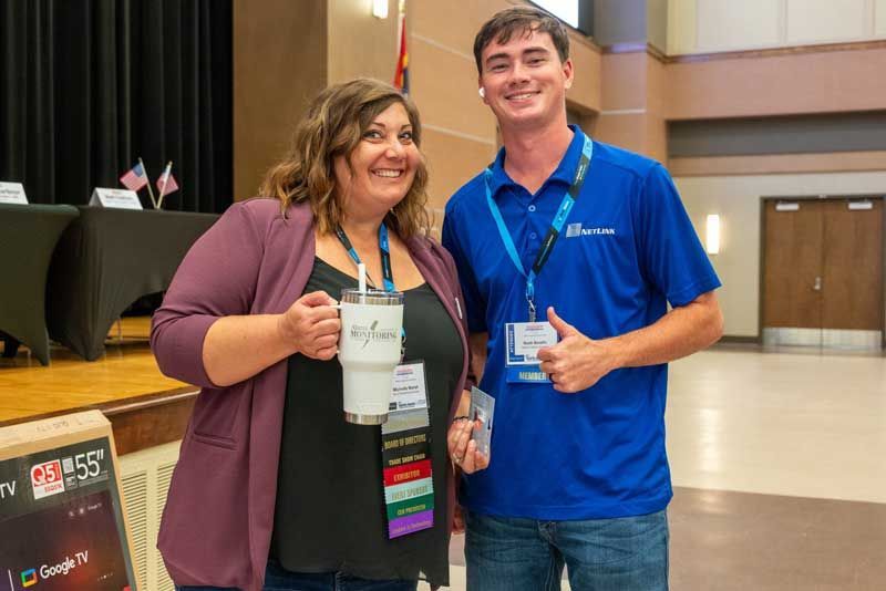 Woman in purple blazer and man in blue polo smiling, holding coffee cups.