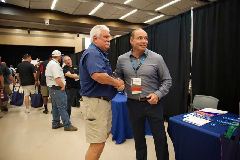 Two men shaking hands in a convention hall.