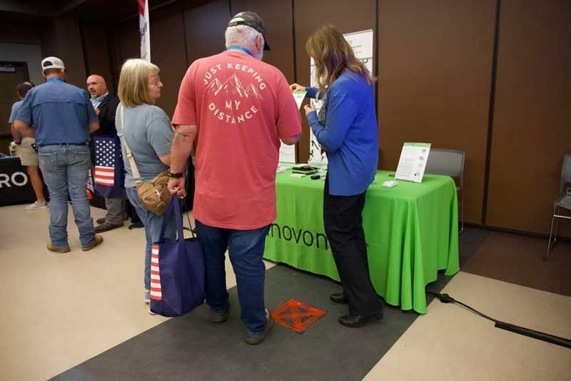 People at a booth. A woman in blue talks to a couple. Red s