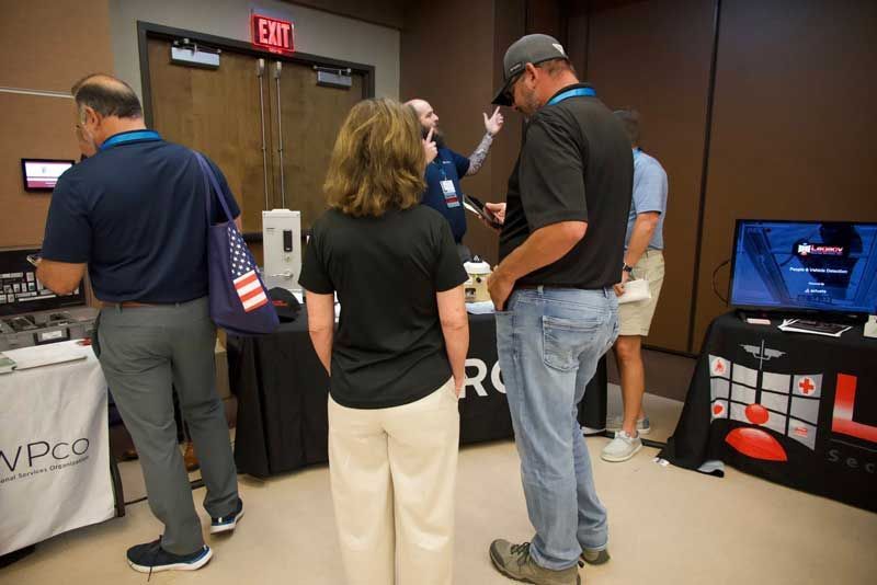 People at a trade show booth, looking at items on a table. 