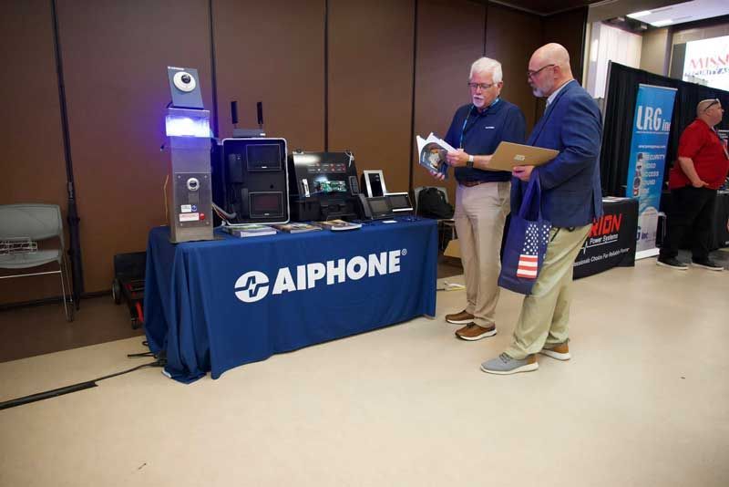 Two men at an Aiphone booth examining materials at a trade show.