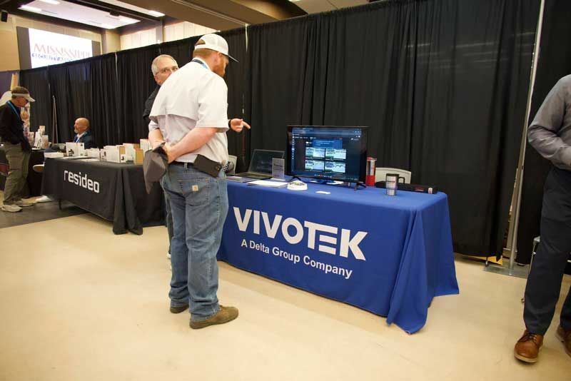 People at a vivotek booth, looking at a monitor. The booth has a blue tablecloth with logo.