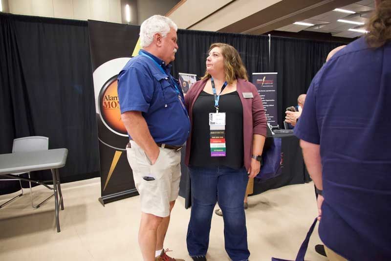 Man in blue shirt and woman in a cardigan talking in an exhibition hall.