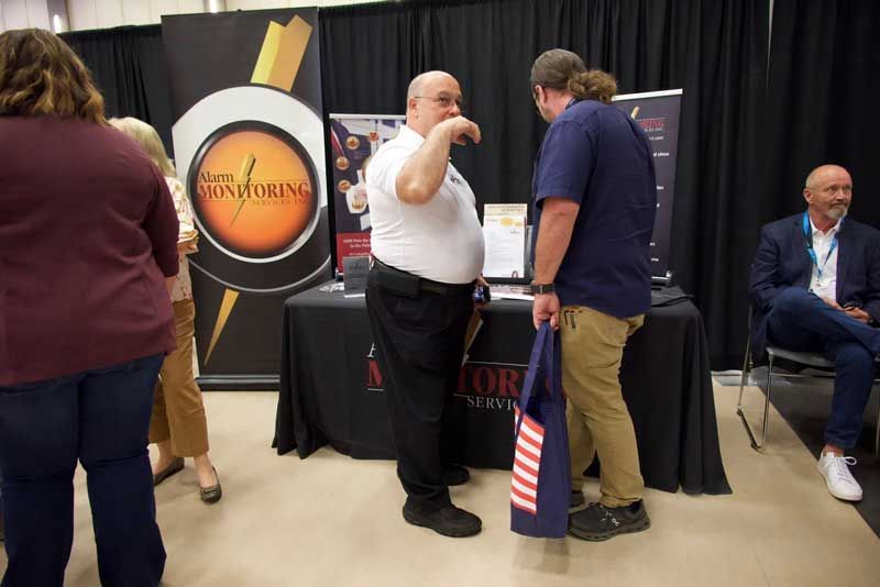 People at a business booth, two men converse near a table with signs. 