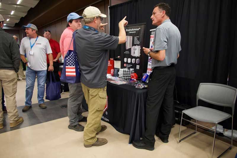 Men at a vendor table, one gesturing at displayed products. 