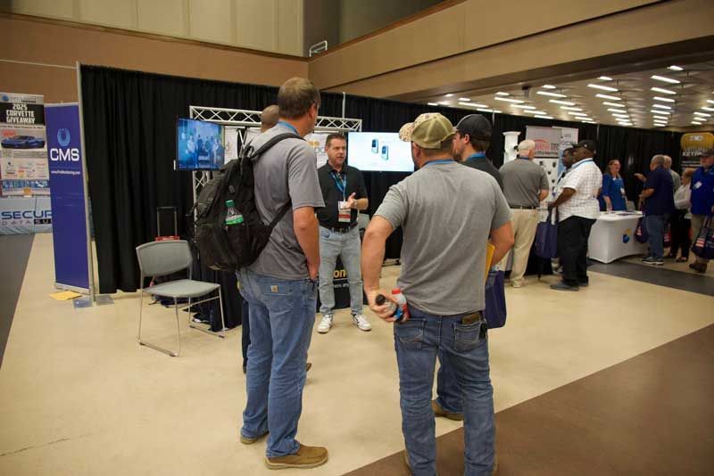 People at a booth in a convention hall, viewing a screen. 