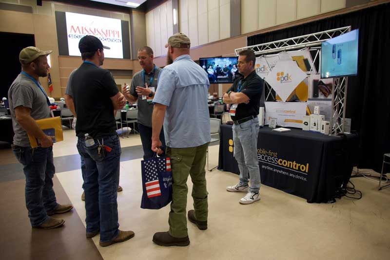 Group of men at a trade show booth, discussing products.