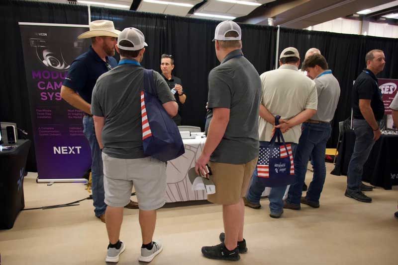People at an event. Some are wearing hats and holding bags. A banner reads 