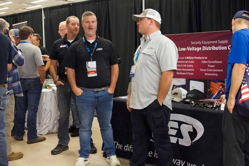 Men at a conference booth; one speaks, the other listens. 