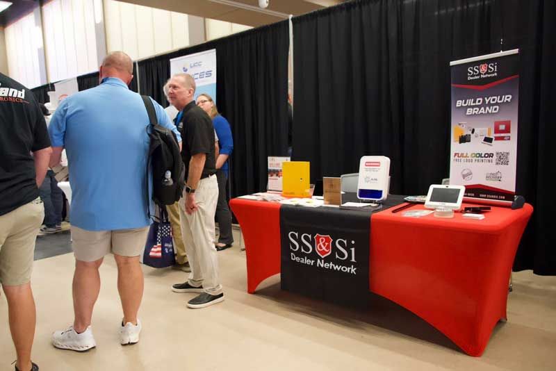 Trade show booth with a red and black table. Three men are standing nearby, conversing.