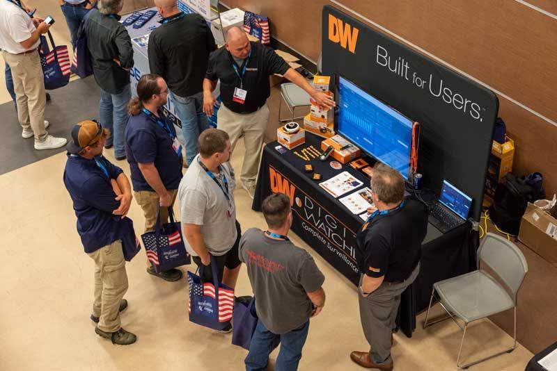People at a trade show booth with a monitor and products, labeled 