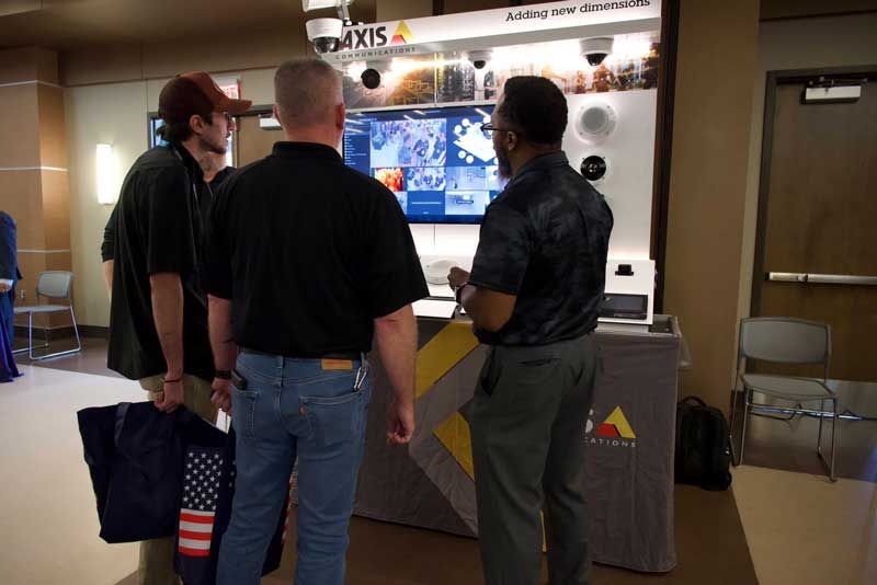 Three men view a security camera display at a trade show. 