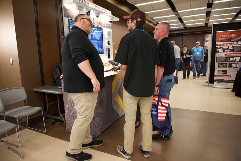 Three men at a display booth in a conference hall. 