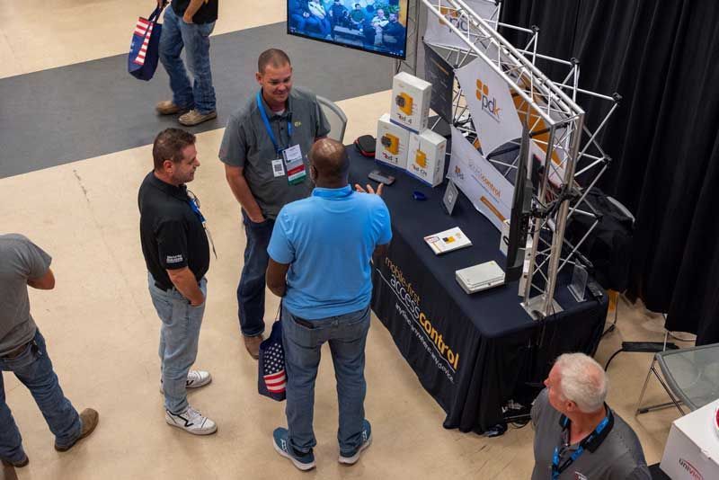 People at a trade show booth, discussing products. Display table with literature.