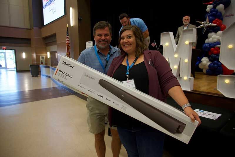 Two people smiling, holding a soundbar box in an event hall. 